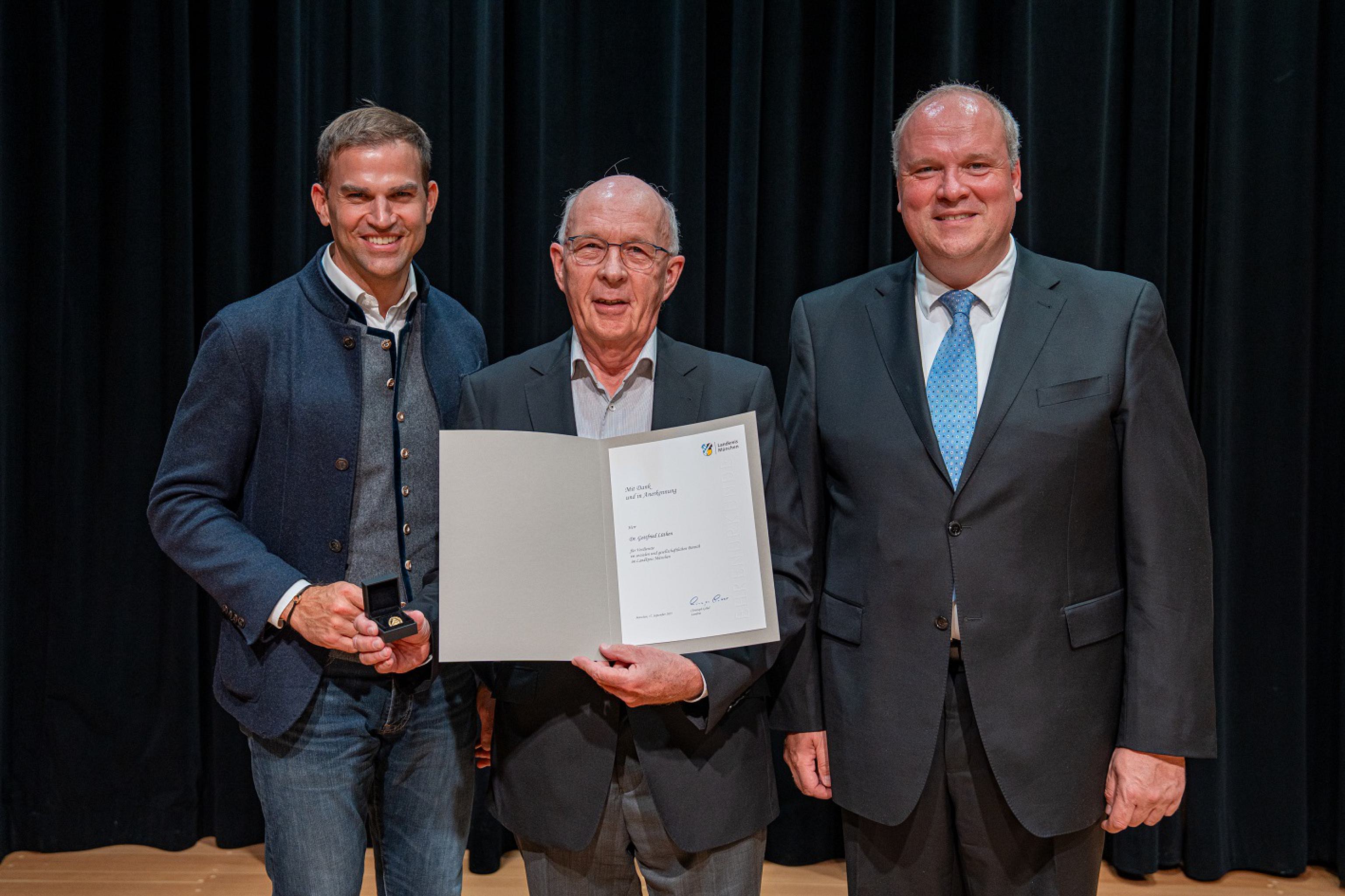 Dr. Gottfried Lüthen hält eine Ehrenurkunde in der Hand. Rechts von ihm steht Landrat Göbel, links von ihm Kirchheims Bürgermeister Maximilian Böltl